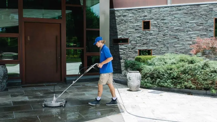 A P&D Power Washing Employee Pressure Washes a Concrete Walkway in Front of a Home.