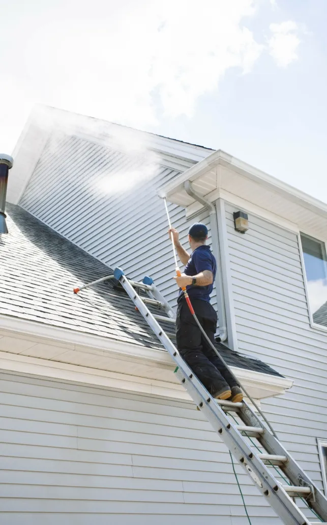 A Man on a Ladder Washes the Roof of a Two Story Home in Canfield.